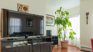 A living room with a flat-screen TV, dark wooden entertainment unit, a potted plant, and a red chair.