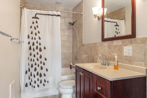 Ein Badezimmer mit Duschvorhang, Toilette, Waschbecken mit Seifenspender und Spiegel.