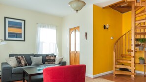 A living room with a grey sofa, a red chair, a wooden staircase, and a yellow wall.