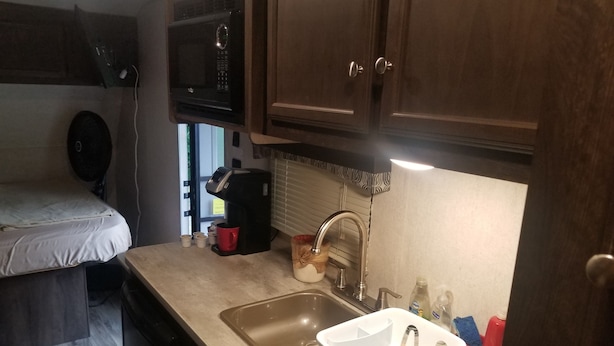 A compact kitchenette with a microwave, coffee maker, sink, and storage containers.