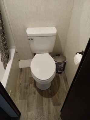 Un bany petit amb un vàter blanc, un terra de fusta i una cortina de banyera.