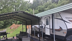A covered outdoor area with a grill and seating, adjacent to a StarCraft RV.