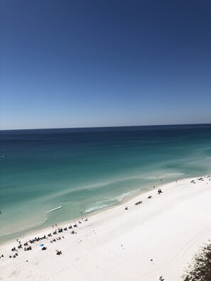 Une plage aux eaux turquoise et limpides, bordée de sable blanc, avec des chaises longues et des parasols.