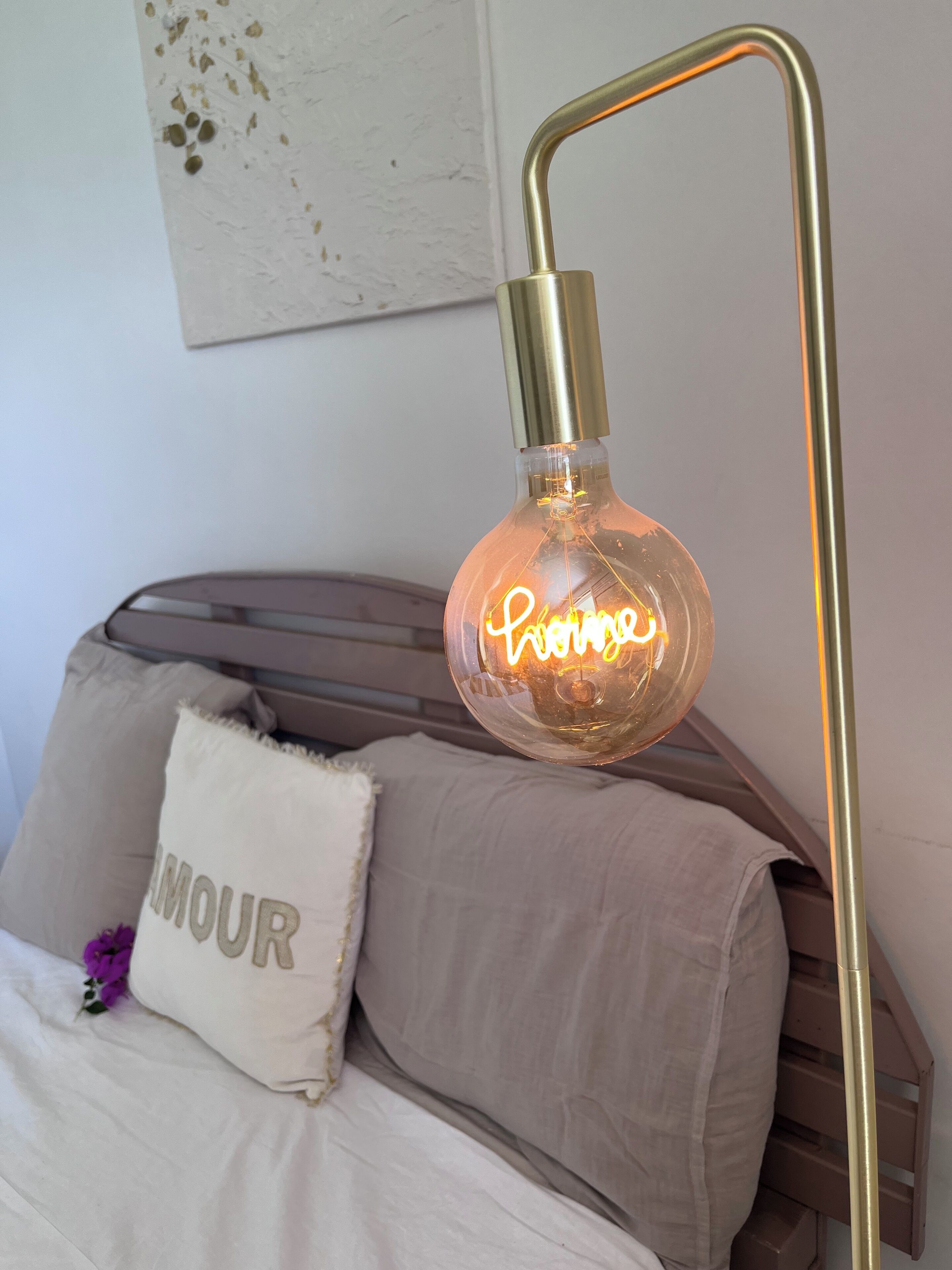 Een bed met hoofdeinde, een bedlampje en een kussen met de tekst 'AMOUR'.