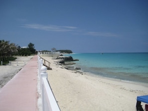 A beach with a paved walkway, a railing, and a view of the ocean. - Blue Beach Front Home at Resort World (North Bimini)