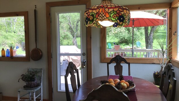 Un comedor con una mesa de madera, sillas, una lámpara colgante de vitral y vistas a un jardín a través de la puerta.
