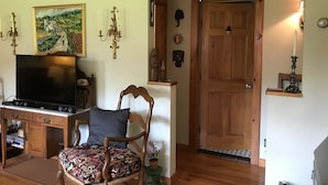 Una sala de estar con un escritorio de madera, un televisor, una silla estampada y un cuadro en la pared.