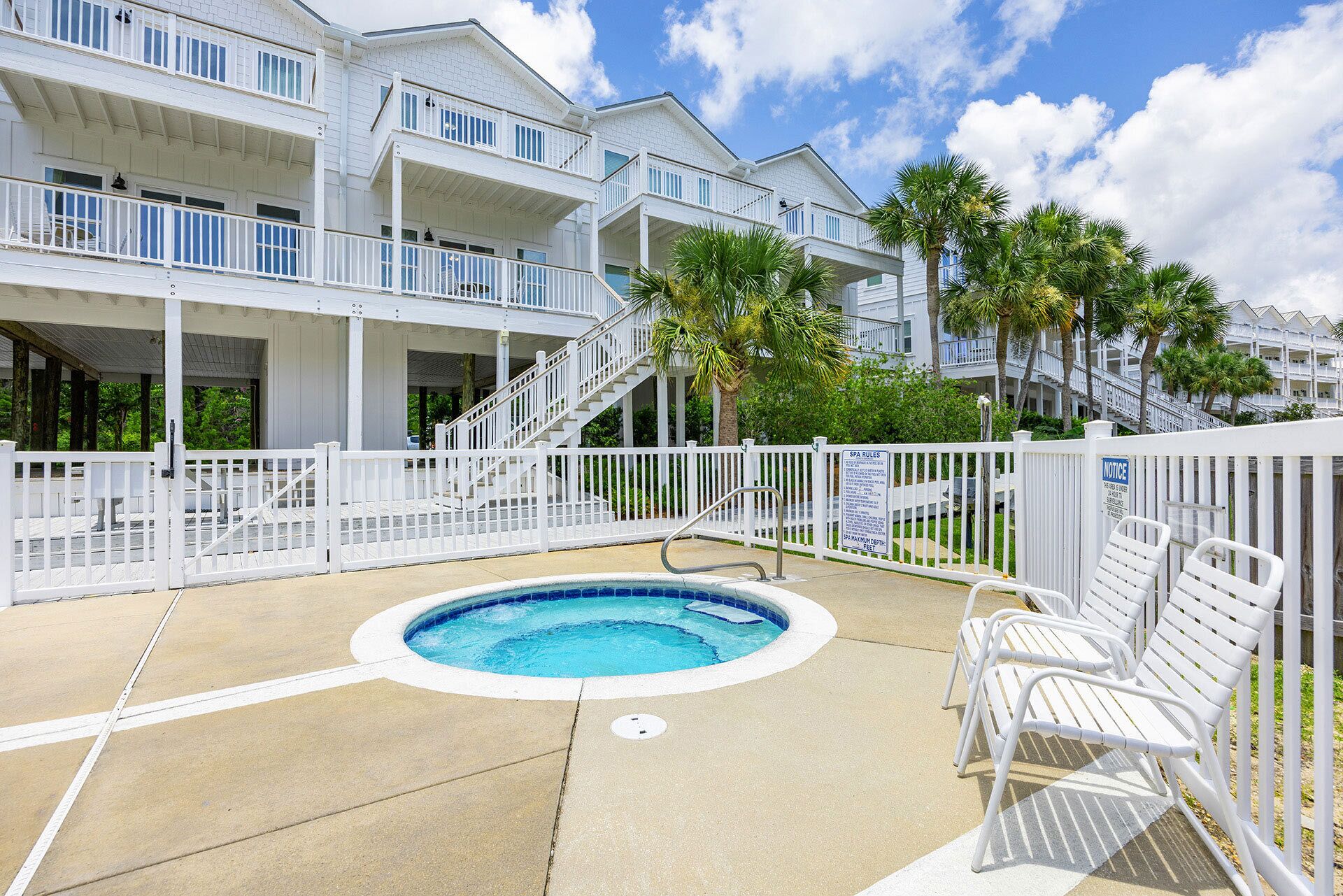 A pool area with a hot tub, white railings, and a staircase leading to a multi-story building with balconies.