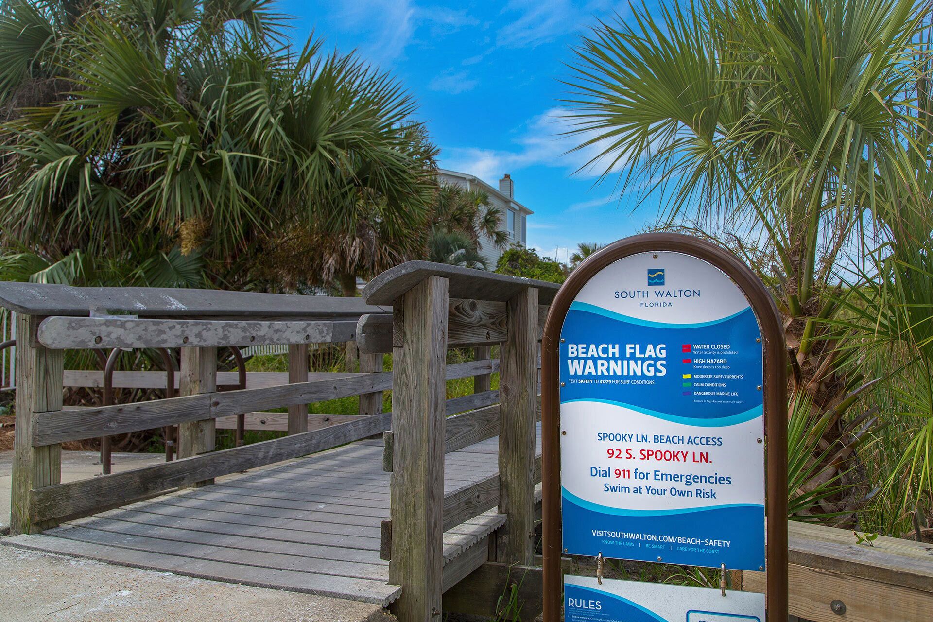 A beach flag warning sign with emergency contact information.