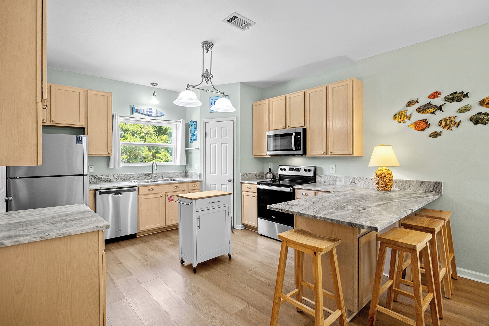 A modern kitchen with wooden cabinets, stainless steel appliances, a marble countertop, and a central island with stools.