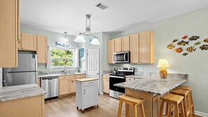 Una cocina moderna con armarios de madera, electrodomésticos de acero inoxidable, encimera de mármol y una isla central con taburetes.