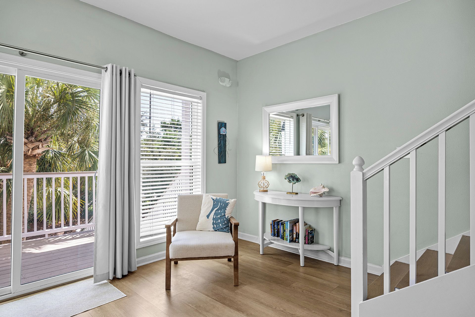 A room with a wooden floor, a white chair, a white console table with a lamp, a mirror, and a bookshelf.