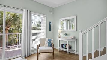 A room with a wooden floor, a white chair, a white console table with a lamp, a mirror, and a bookshelf.