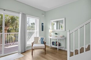 A room with a wooden floor, a white chair, a white console table with a lamp, a mirror, and a bookshelf.