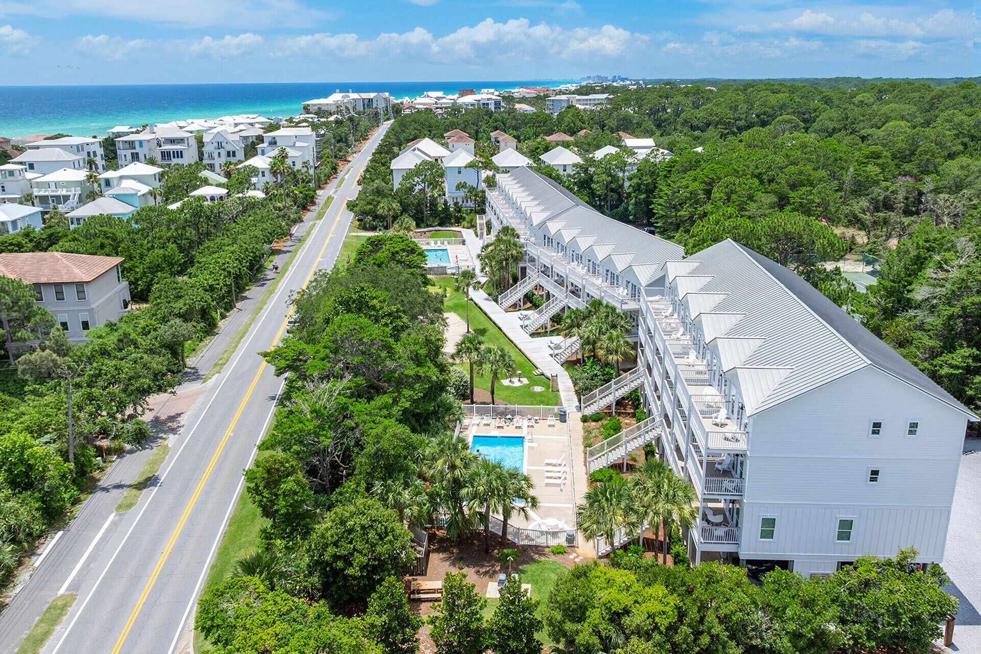 Un complexe hôtelier comprenant un long bâtiment, une piscine et une route menant à la plage.
