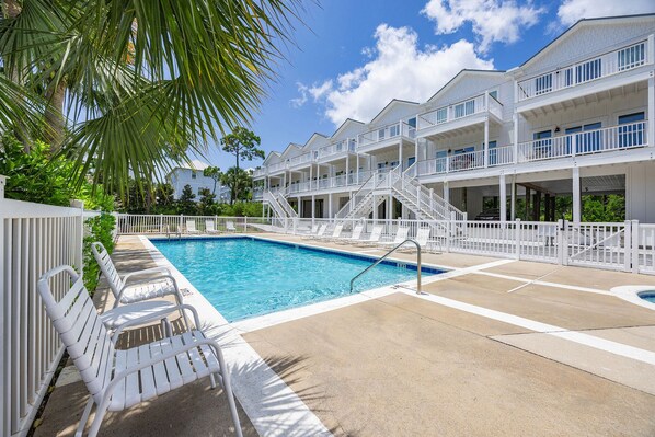 A pool area with white pool chairs, a clear blue pool, and a multi-story building with balconies.