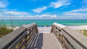 Un paseo marítimo de madera que conduce a una playa con agua turquesa cristalina y un cielo azul brillante.