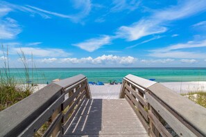 A wooden boardwalk leading to a beach with clear turquoise water and a bright blue sky.