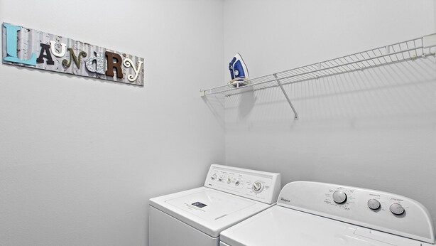 Un cuarto de lavandería con dos lavadoras Whirlpool blancas, un letrero de metal con letras y un planchador azul sobre un tendedero.