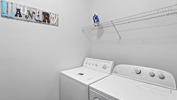 A laundry room with two white Whirlpool washers, a metal sign with letters, and a blue iron on a drying rack.