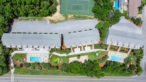 Un hotel grande con varias piscinas, canchas de tenis y una carretera en primer plano.