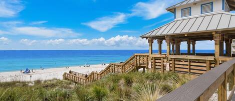 A beach view with a wooden boardwalk leading to a building with a metal roof.