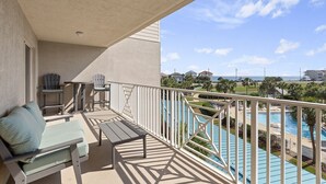 Een balkon met uitzicht op een zwembad en de oceaan. Er staan twee Adirondack-stoelen en een klein tafeltje.