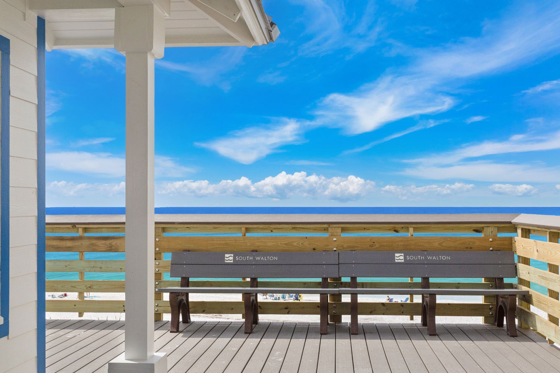 Eine Holzterrasse mit zwei Bänken, auf denen 'South Walton' steht, mit Blick auf einen Strand.