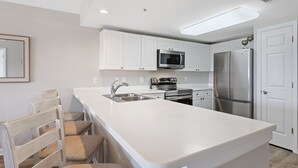 Een moderne keuken met witte kasten, roestvrijstalen apparatuur en een groot eiland met barkrukken.