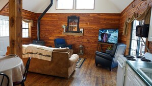 Un interior de cabaña acogedor, con revestimiento de madera, chimenea, televisor y comedor.