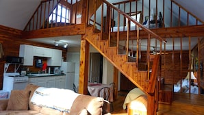 Un amplio espacio de sala de estar con una escalera de madera, una cocina con gabinetes blancos y una zona de estar acogedora con un sofá y sillas.