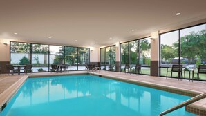 An indoor swimming pool with clear views of the outdoors, surrounded by chairs and tables. - Courtyard by Marriott Ames (Ames)