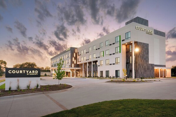 Un hotel Courtyard by Marriott con diseño moderno, que cuenta con una entrada amplia, varios pisos y un área exterior bien cuidada.