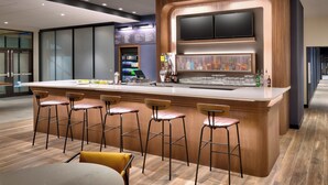 A modern bar area with a wooden bar counter, multiple stools, a large flat-screen TV mounted above the counter, and a well-lit interior. - Courtyard by Marriott Ames (Ames)