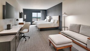A modern hotel room with a large bed, a desk, a chair, a sofa, and a view of the city. - Courtyard by Marriott Ames (Ames)