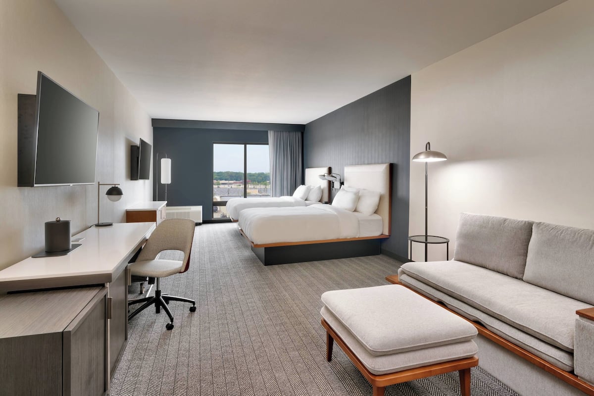 A modern hotel room with a large bed, a desk, a chair, a sofa, and a view of the city.