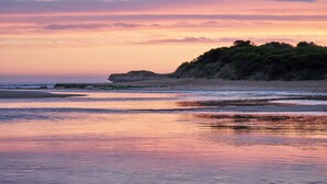 Una playa con un promontorio rocoso y un mar tranquilo al atardecer.