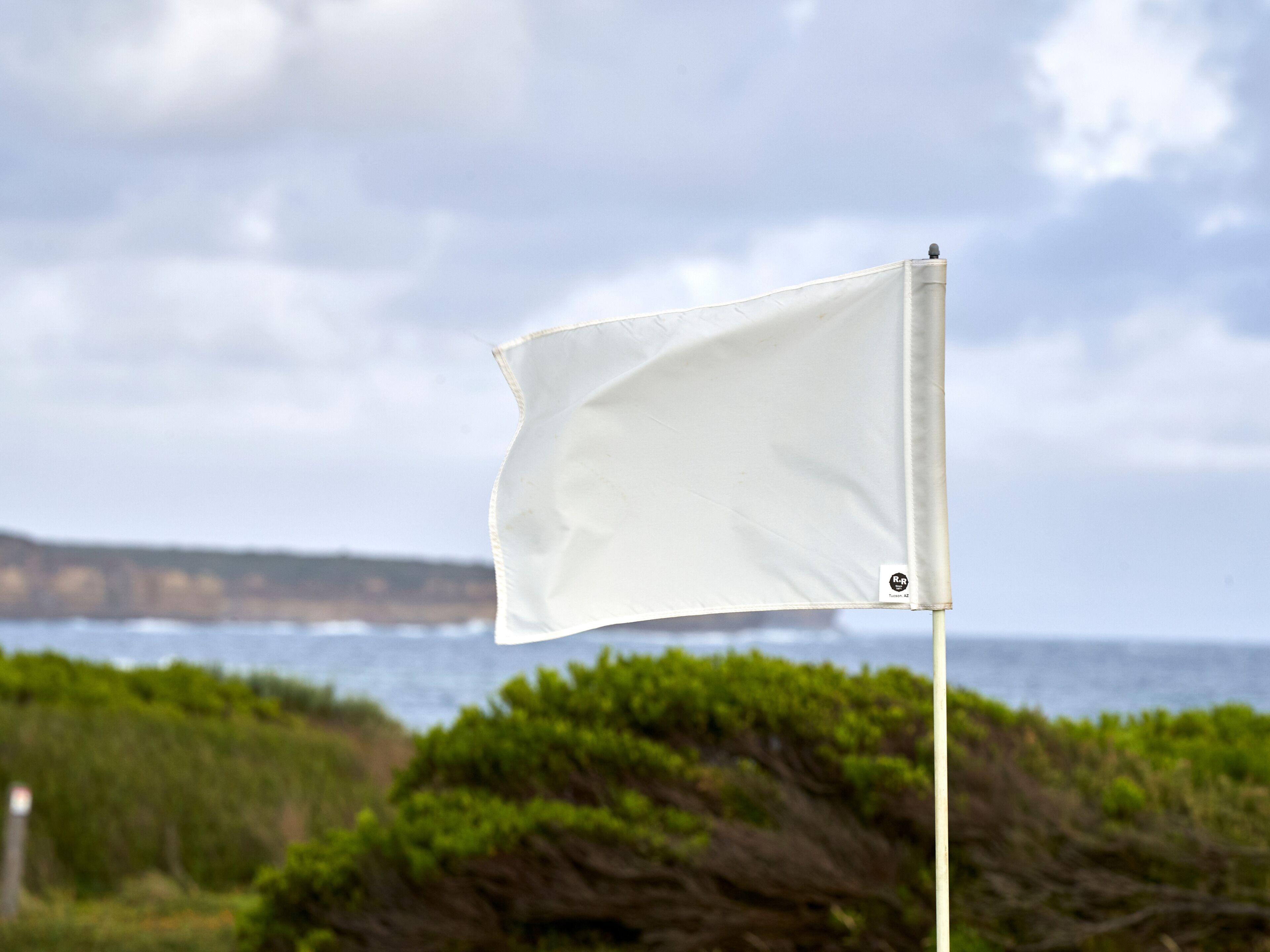 Una bandera blanca en un asta con un paisaje costero al fondo.