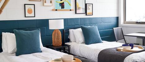 A hotel room with two beds, a window, and artwork on the wall.