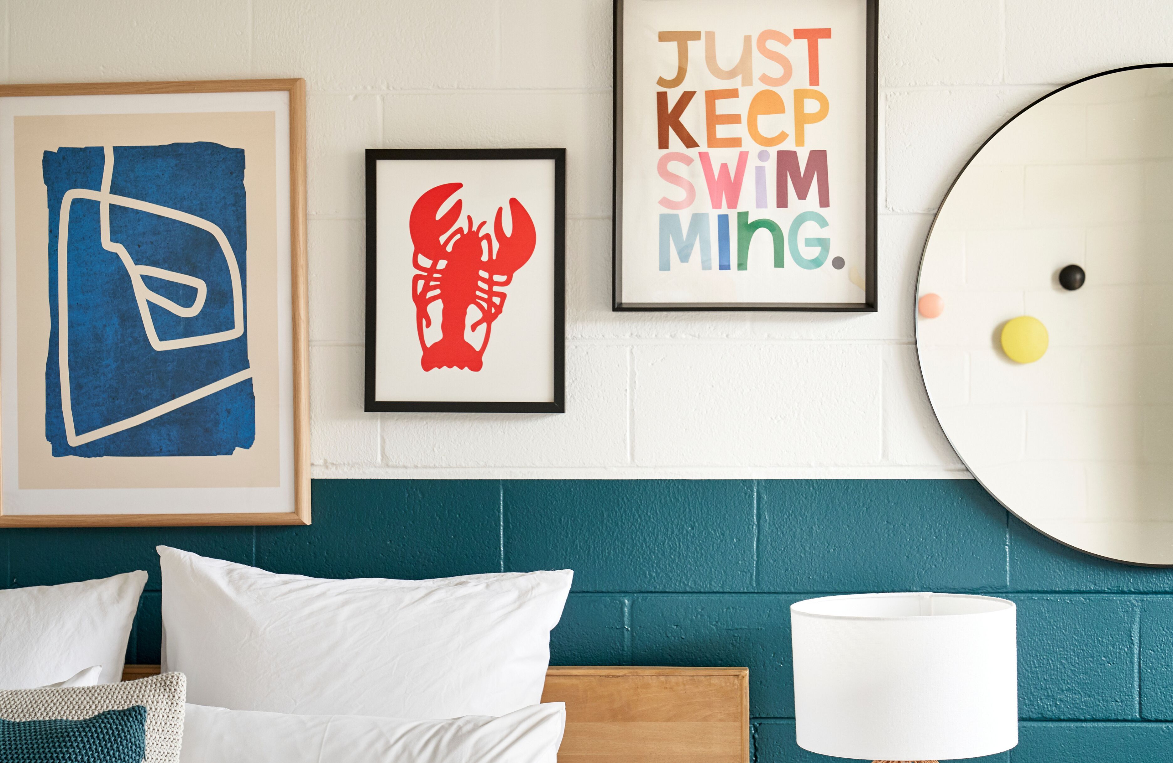 Un dormitorio con cabecera color turquesa, ropa de cama blanca y tres cuadros en la pared.