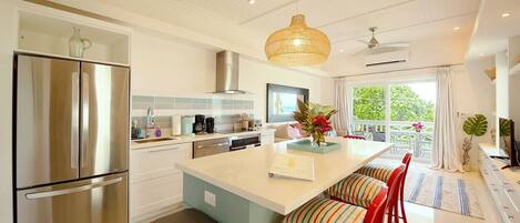 A modern kitchen with stainless steel appliances, a central island with bar stools, and a view to the outdoors.
