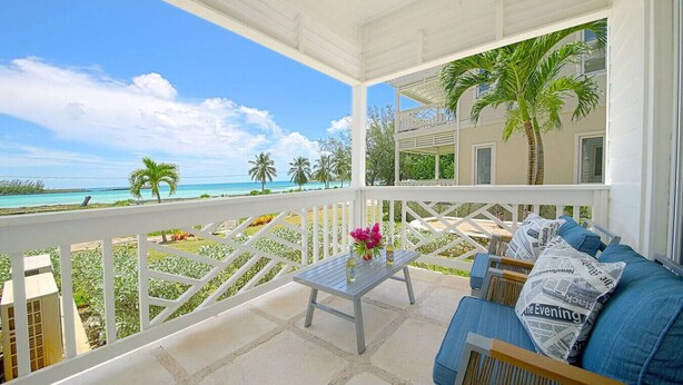 Ein überdachter Balkon mit Blick auf den Ozean, ein Tisch mit Blumen und eine Couch mit Kissen.