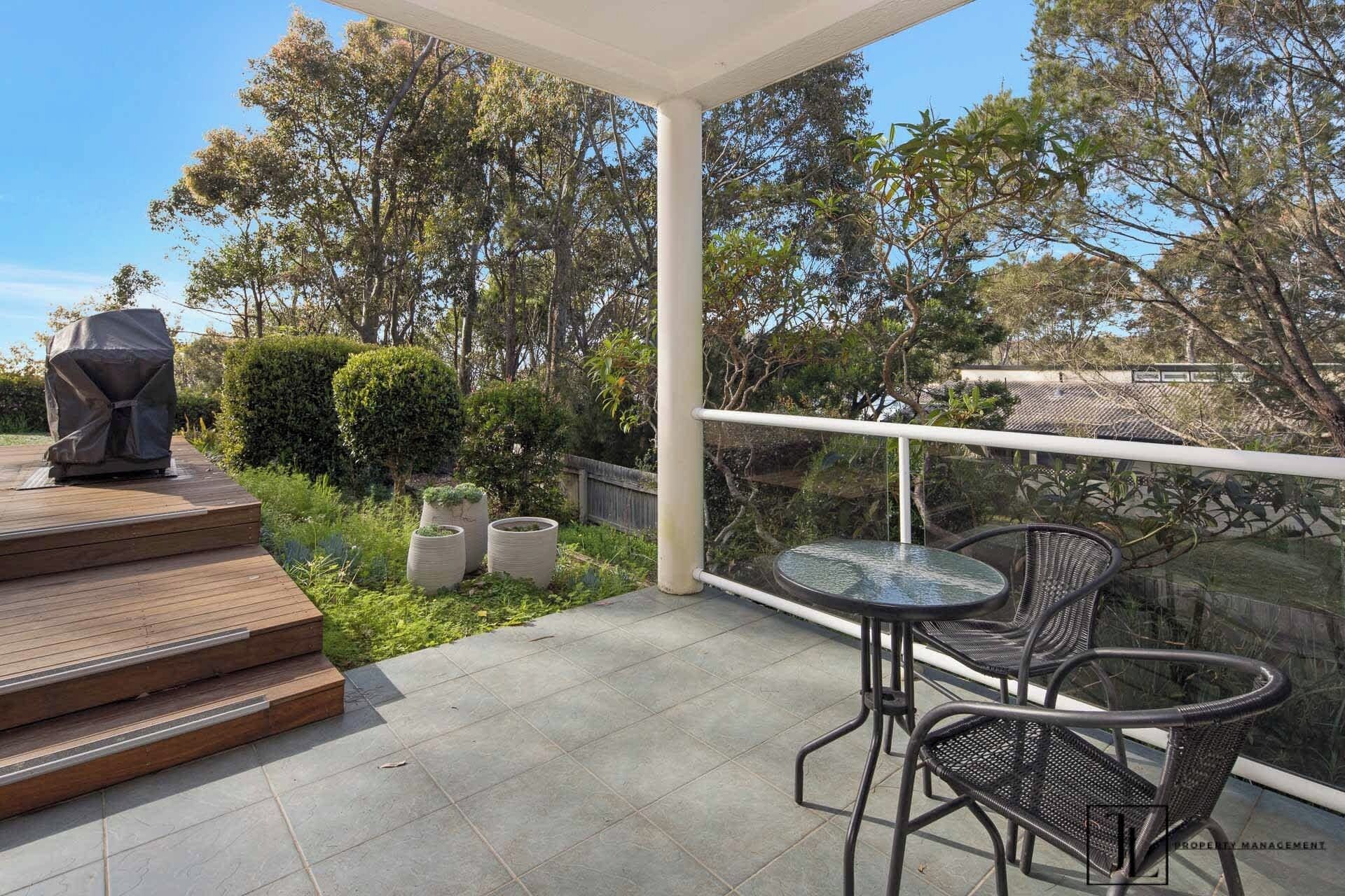 A covered patio with a table and chairs, a barbecue grill, and a view of the surrounding trees and garden.