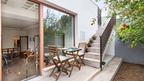 An outdoor dining area with a table and chairs, a staircase, and a glass door leading to an interior space.