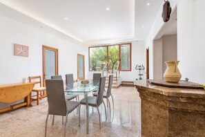 A modern dining area with a glass table, metal chairs, and a wooden bench. - SA LLIMONERA - Charming town house with patio and garden Free WiFi (Sant Llorenç des Cardassar)