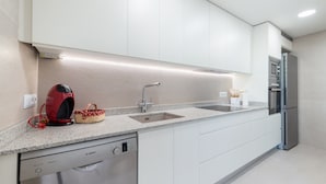A modern kitchen with white cabinets, a stainless steel dishwasher, a double sink, and a built-in oven.