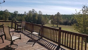 Une terrasse en bois, aménagée avec du mobilier d’extérieur, notamment des chaises et une table, qui offre une vue sur un paysage boisé.