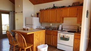 Une cuisine avec des meubles de rangement en bois, un réfrigérateur blanc, une cuisinière et une table à manger en bois, accompagnée de chaises.