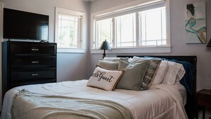 A bedroom with a bed, a dresser, a TV, and two windows.