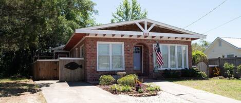 A single-story brick house with a gabled roof, a front porch, and an American flag.